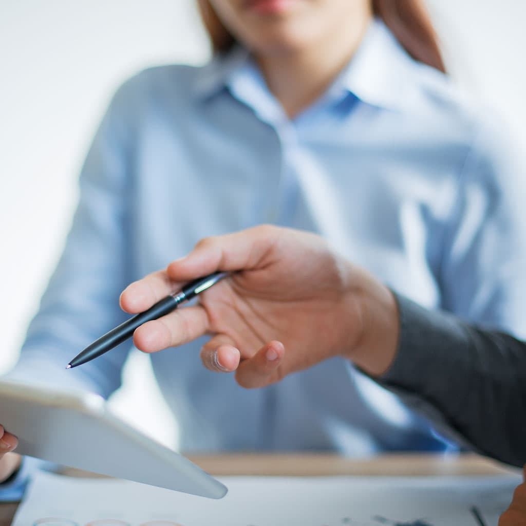 Dos personas discuten información en una tableta durante una sesión de asesoría en Sevilla. Una mano sostiene un bolígrafo y hace gestos hacia la tableta, mientras la otra persona escucha atentamente.